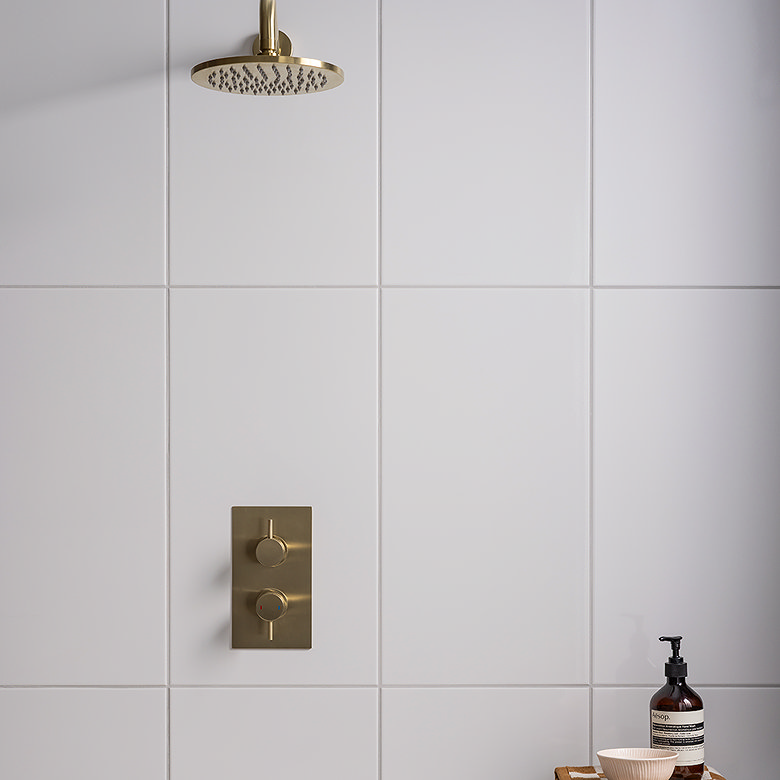 White shower tiles with matching white grout creating a seamless finish, contrasted with brushed brass shower fittings