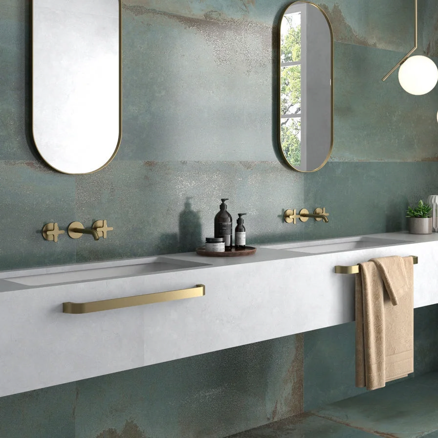 Large-format blue-green bathroom wall tiles with a textured metallic finish behind a double vanity and brushed brass taps
