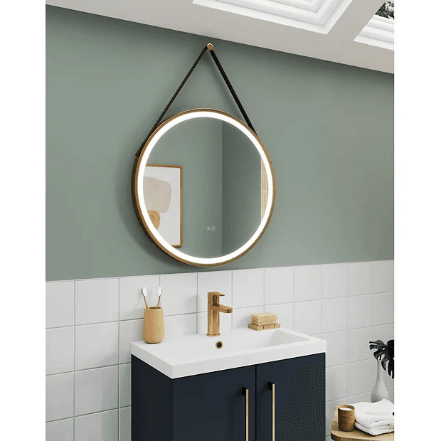 Round illuminated mirror on sage green and white tiled wall with navy vanity unit