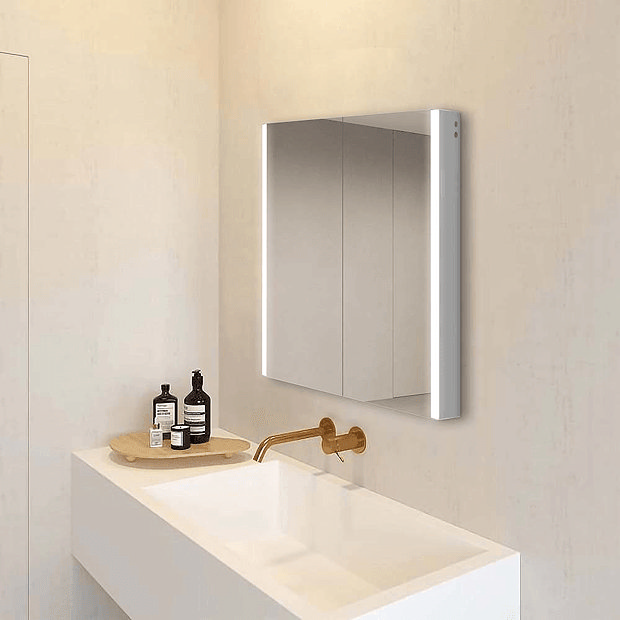 Illuminated mirrored cabinet on cream wall with wall mount brass tap and white basin