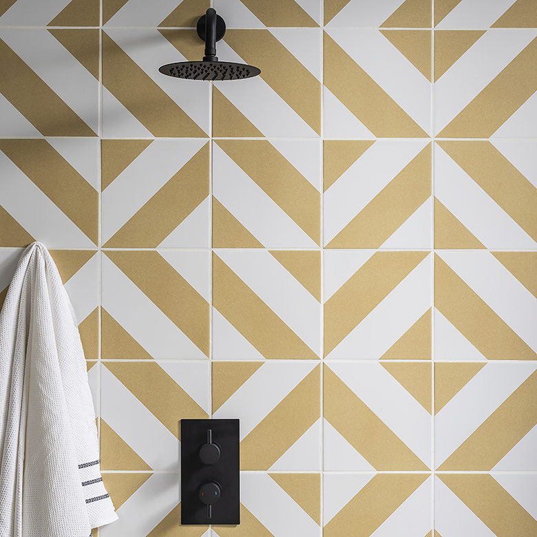 Bathroom wall with geometric yellow and white tiles, featuring a modern black shower control panel. A soap dish and white towel add subtle accents to the minimalist design.