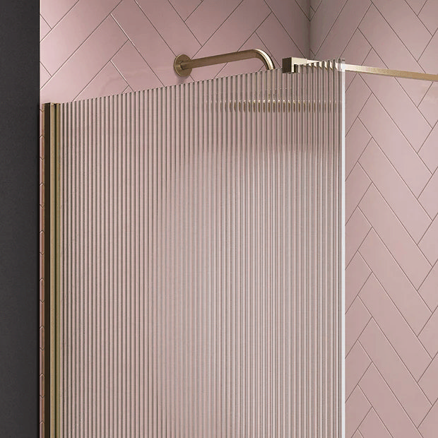 Fluted shower screen with brass frame against pink tiles