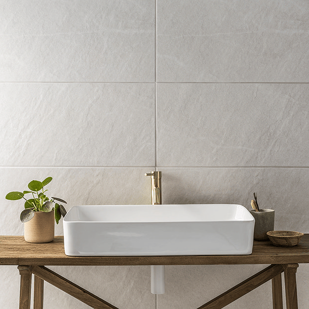White stone tiles behind countertop basin with brass tap