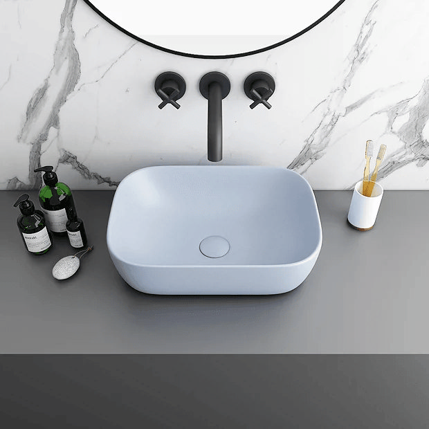 Blue basin on grey counter with black taps and marble wall