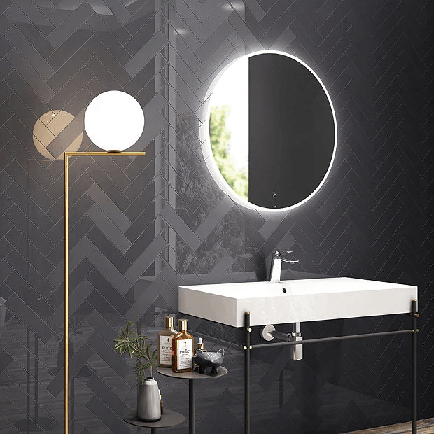 Black herringbone wall tiles with illuminated mirror and brass lamp