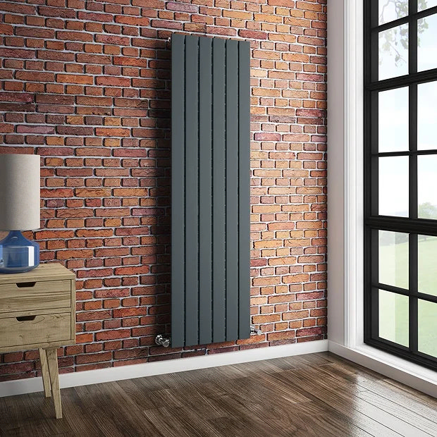 Grey vertical radiator on brick wall