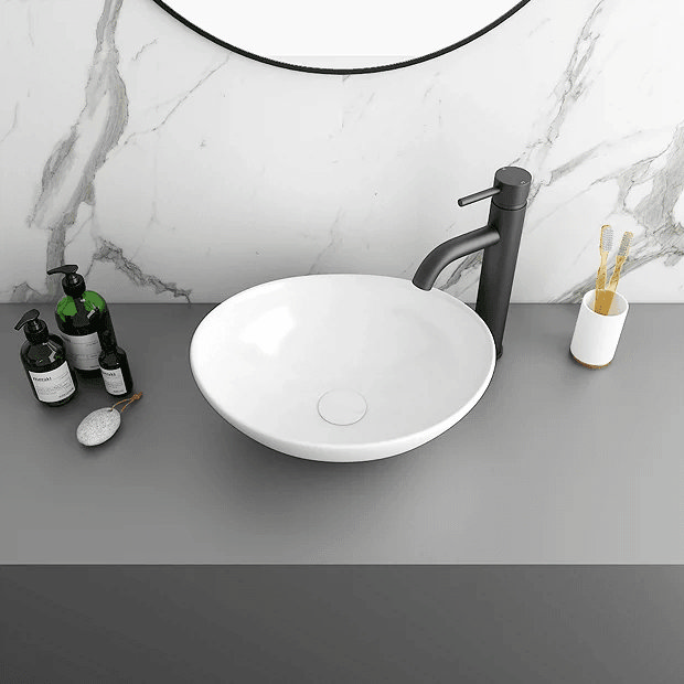 White basin on grey counter with black tap and marble wall