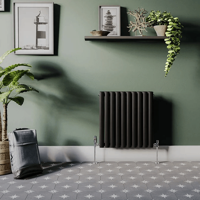 Black panel radiator mounted on sage green wall and grey floor tiles