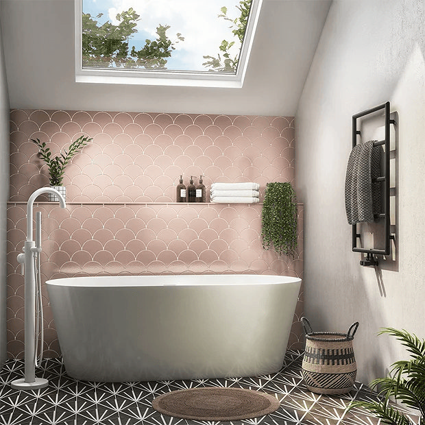 Pink fish scale tiles behind bath under a skylight 