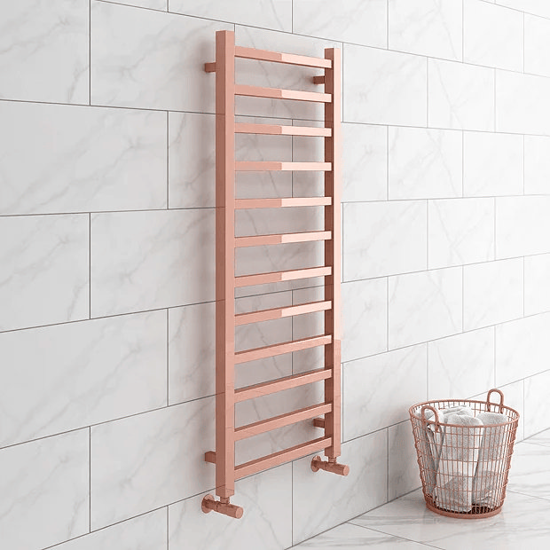 Rose gold heated towel rail on white marble tiles