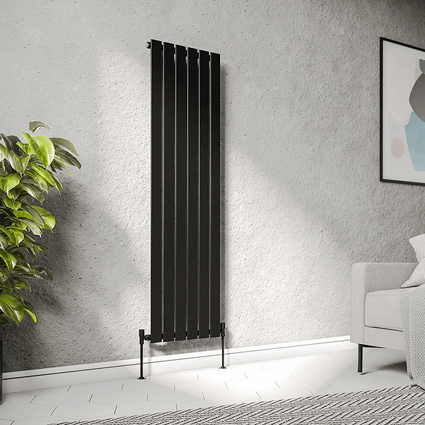 Vertical matt black radiator on white stone wall with floor plant