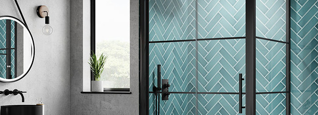 Modern bathroom with a teal herringbone tiled shower enclosure featuring black framed glass doors and minimalist accents.