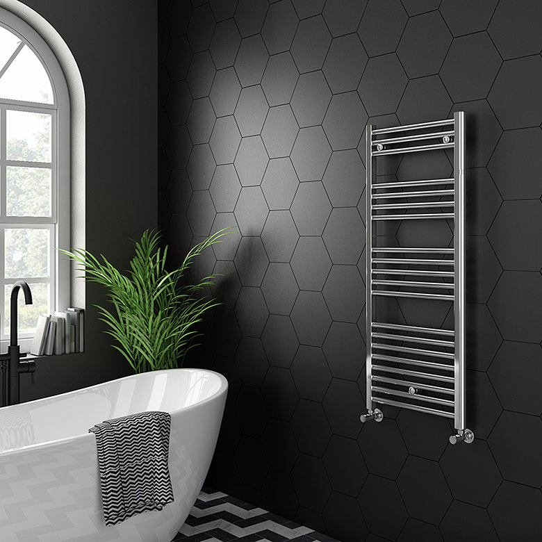 Chrome heated towel rail mounted on a black hexagon-tiled wall beside a freestanding bath