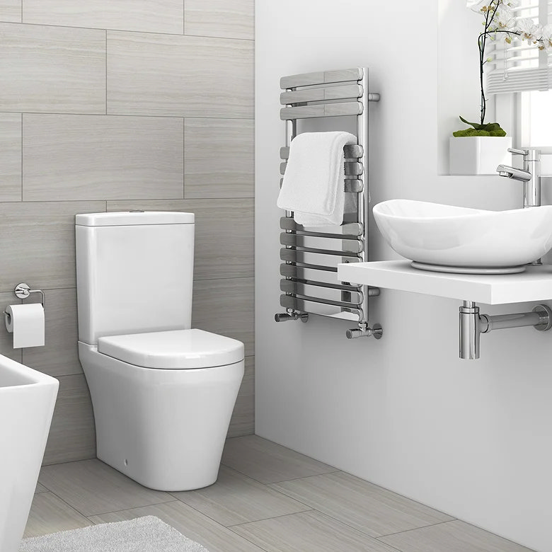 Chrome heated towel rail with a white towel mounted beside a basin and toilet in a modern bathroom