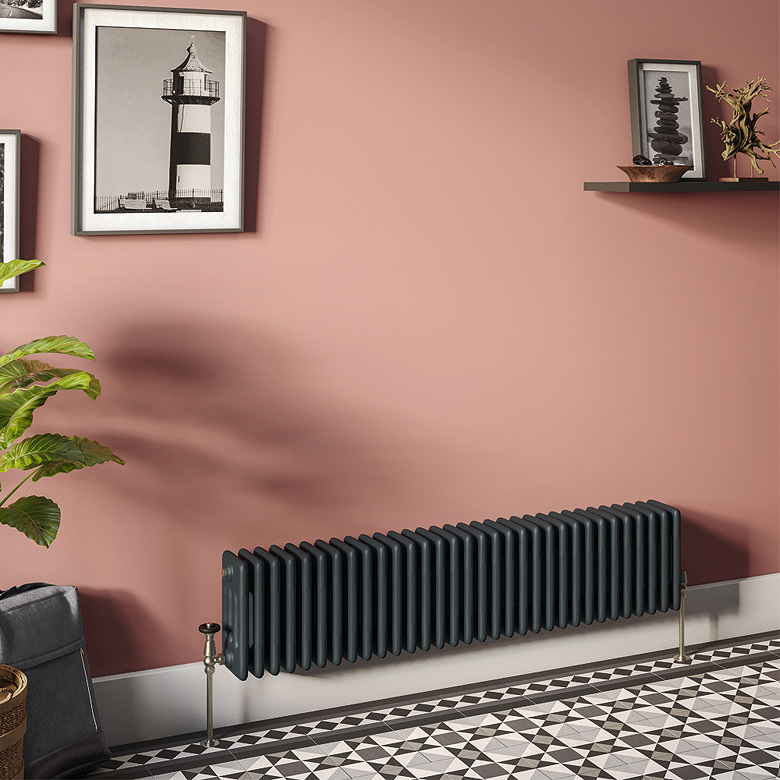 Traditional black horizontal column radiator mounted against a pink wall above patterned floor tiles