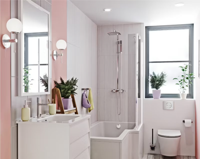 Soft pink and white bathroom featuring a modern bathtub with overhead shower, sleek white vanity, and potted plants by the window for a fresh, serene space.