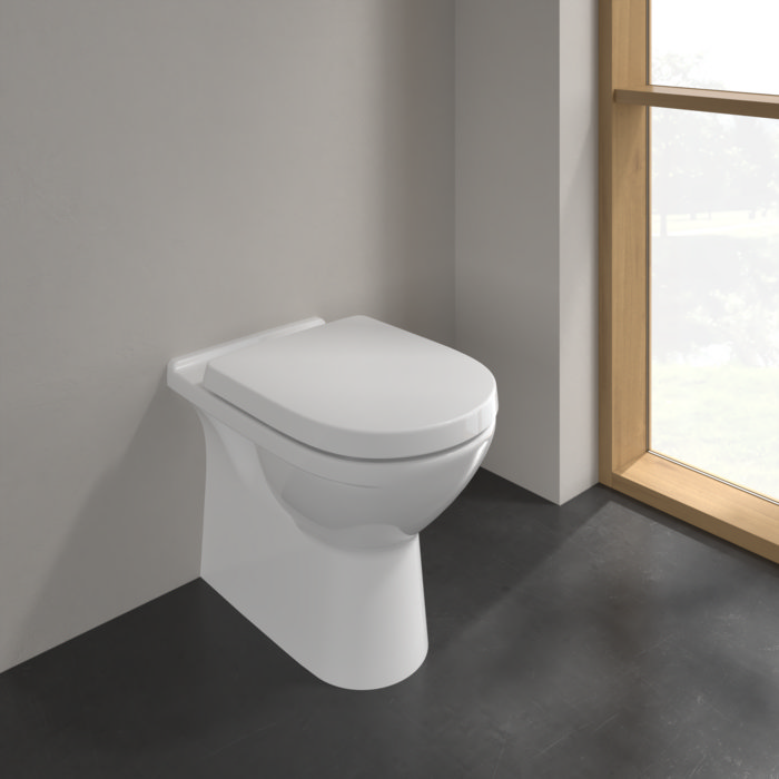 Modern back-to-wall toilet with a minimalist design, featuring a sleek white seat and concealed cistern, set against a neutral-toned bathroom with natural light from a large window.