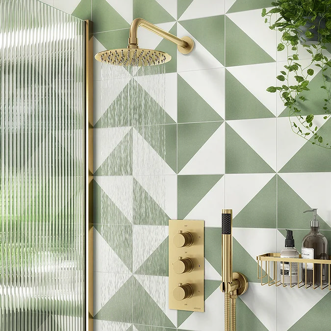 Geometric green and white feature wall with a brushed brass rainfall showerhead and matching shower valve. The fluted glass shower screen and gold shower accessories add elegance, while greenery enhances the fresh, modern look.