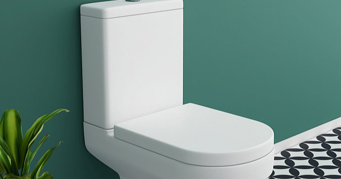 Close-coupled toilet with a modern design set against a teal bathroom wall, accompanied by a patterned black and white floor tile for a contemporary look.