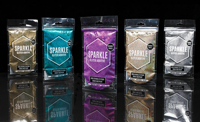 Five packets of Sparkle Glitter Additive in various colors, including gold, turquoise, purple, and silver, displayed on a reflective surface against a black background.