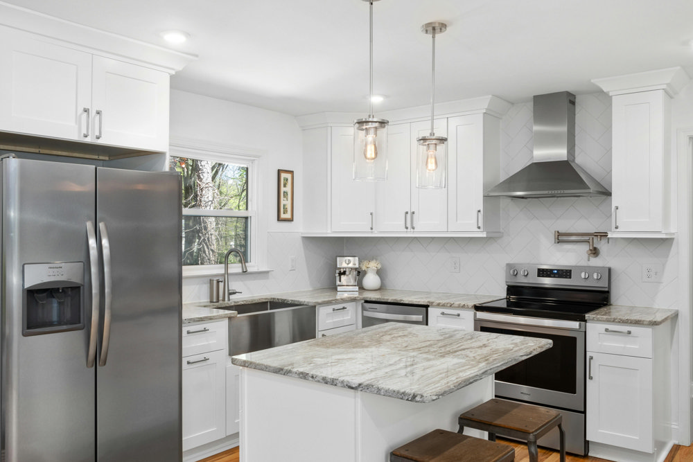 Modern white kitchen with granite countertops, stainless steel appliances, and island seating under pendant lighting