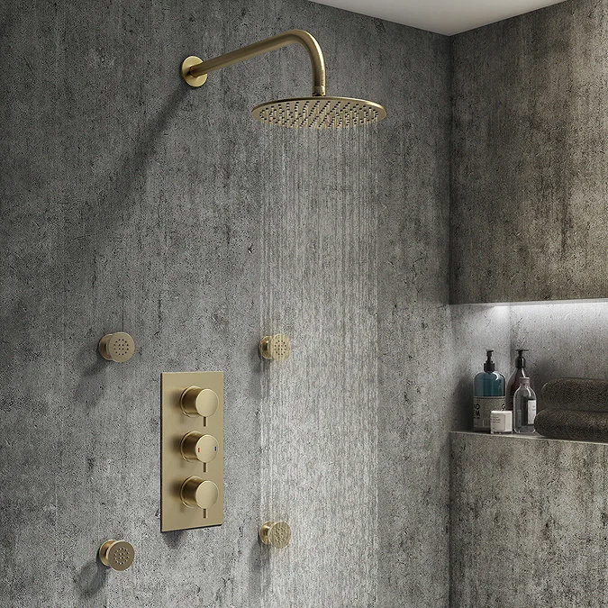 Modern wet room featuring a brushed brass rainfall shower head, matching body jets, and textured concrete effect wall tiles, creating a luxurious and industrial-inspired bathroom.