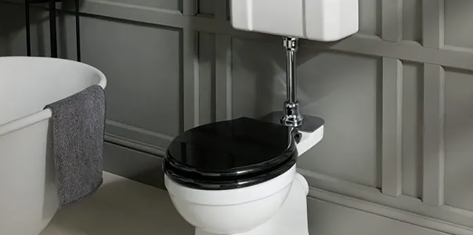 Close-up of a traditional high-level toilet with a sleek black seat and chrome flush pipe, set against a grey panelled wall in a classic bathroom.