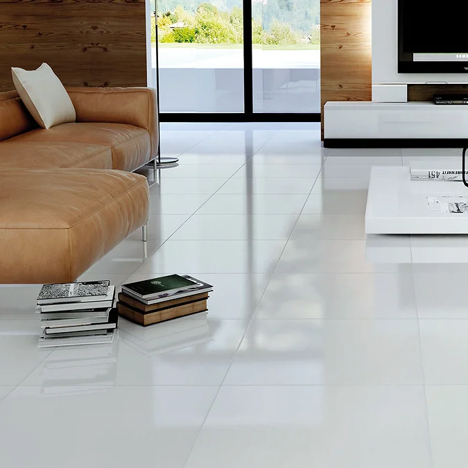 Glossy white floor tiles in a modern living room with a tan leather sofa, a low white coffee table, and large glass doors overlooking a scenic view.