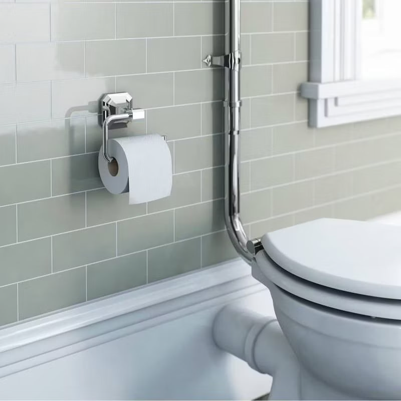 Chrome toilet roll holder mounted on a green tiled bathroom wall next to a toilet