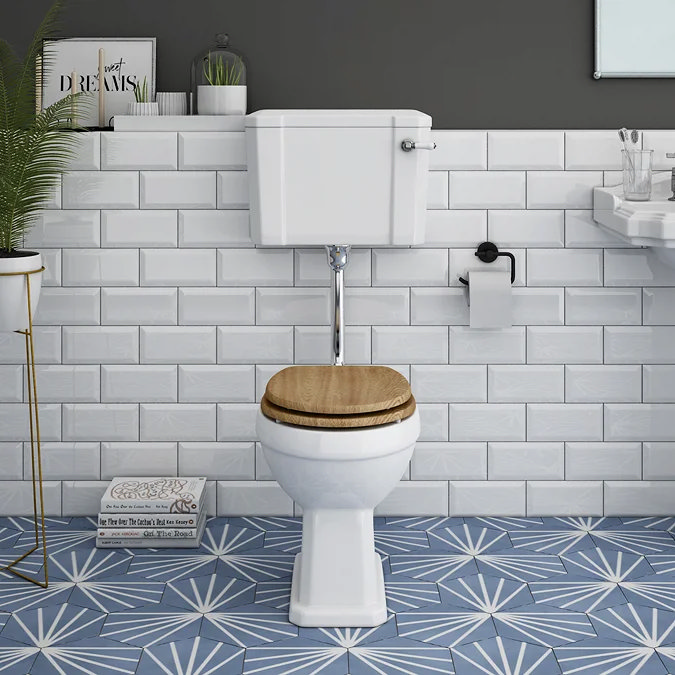 Low-level toilet with wood effect seat in a small bathroom with blue patterned floor tiles and white subway tiles