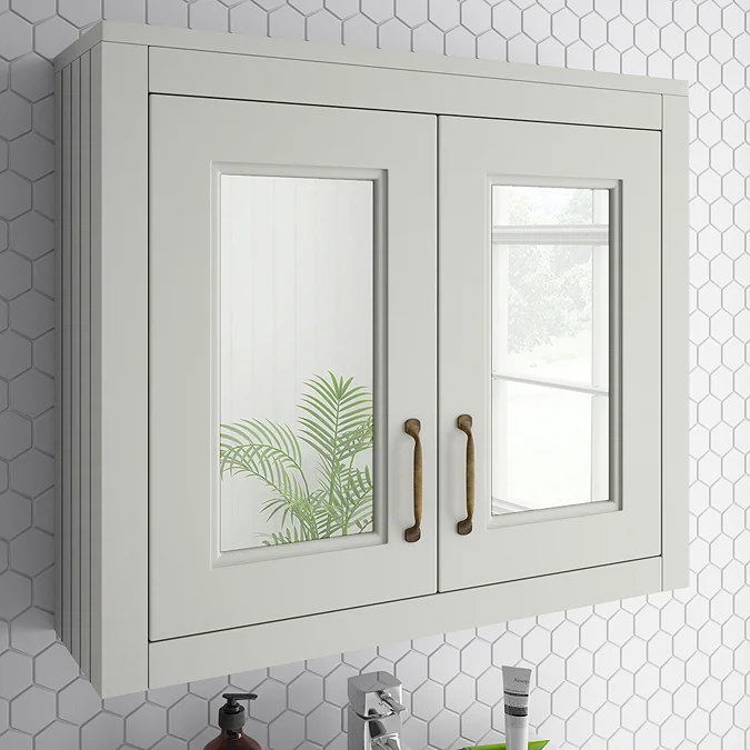 White bathroom cabinet with mirrored doors and brass handles against hexagonal tile wall