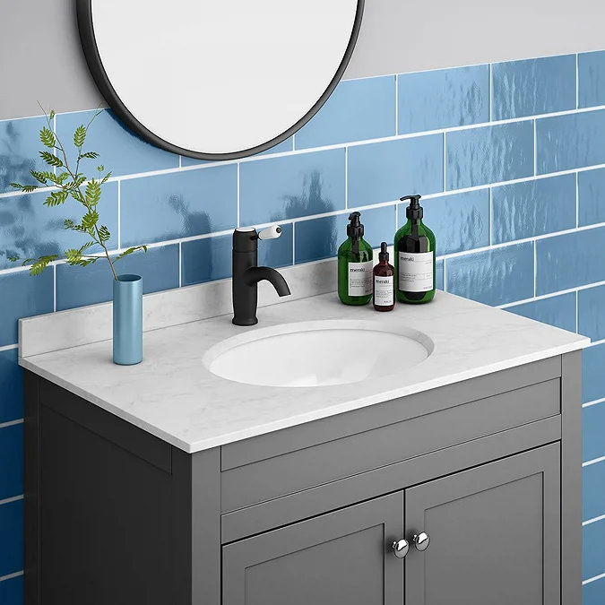 Grey vanity unit with white countertop and oval inset basin beneath round mirror and blue tiled wall.