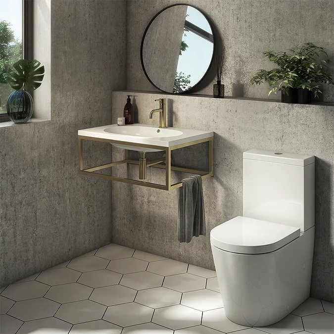 Modern cloakroom with wall-mounted basin on brushed brass frame and white close-coupled toilet against concrete-effect walls.