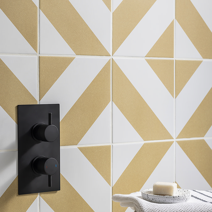 {Bathroom wall with geometric yellow and white tiles, featuring a modern black shower control panel. A soap dish and white towel add subtle accents to the minimalist design.ALT TEXT HERE}