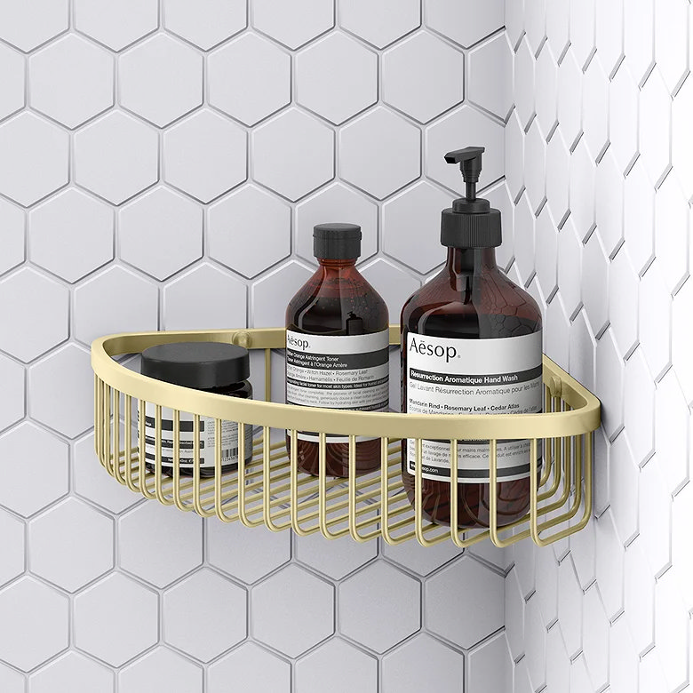 Brushed brass wire corner shower basket holding soap bottles in a tiled shower