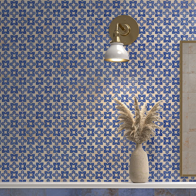 Blue and beige floral-patterned bathroom wall tiles with a brass wall light and a decorative vase.