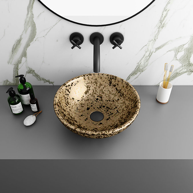 Speckled stone vessel basin with a black wall-mounted tap set against a marble backsplash, complemented by minimalistic bathroom accessories on a sleek grey countertop.