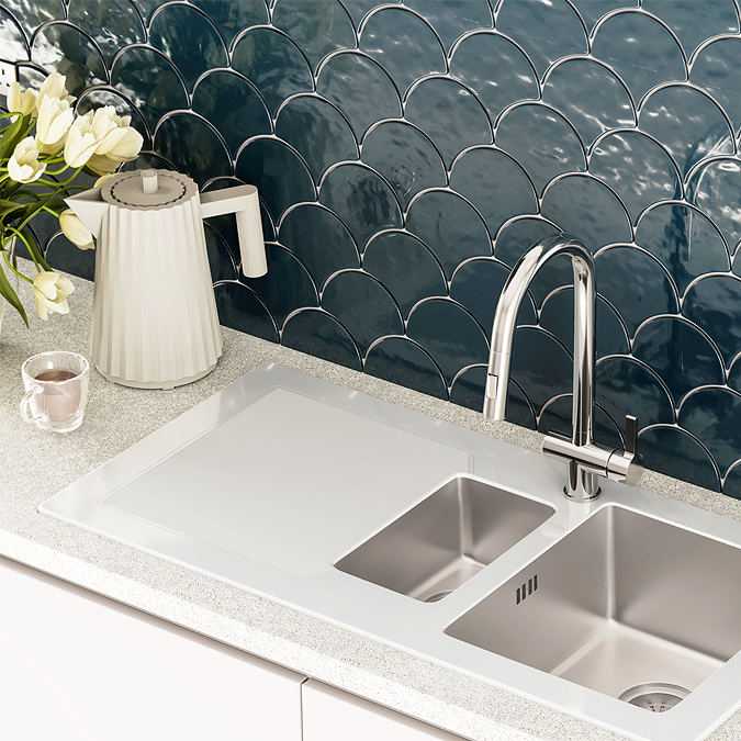 Modern kitchen sink with a chrome faucet, white countertop, and blue fish-scale tile backsplash, decorated with white flowers and a cream-colored kettle.