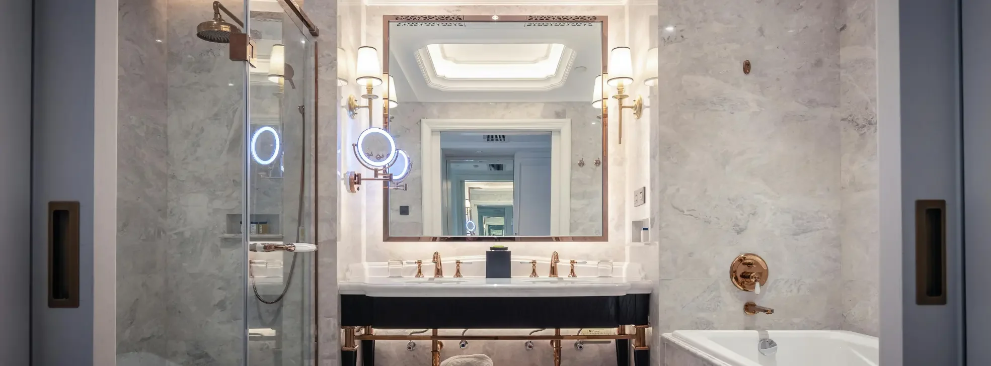 Luxury en-suite bathroom with a large backlit mirror, dual gold taps, marble walls, and built-in lighting for a refined hotel-style finish.