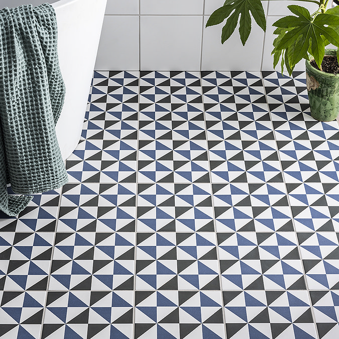 Blue, black, and white geometric pattern floor tiles in a bathroom with a white bathtub and green potted plant, adding a bold, modern touch.