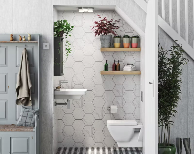 Compact under-stairs bathroom with hexagonal tiles, floating shelves adorned with colourful plants, and a wall-hung toilet, creating a fresh and space-saving design.