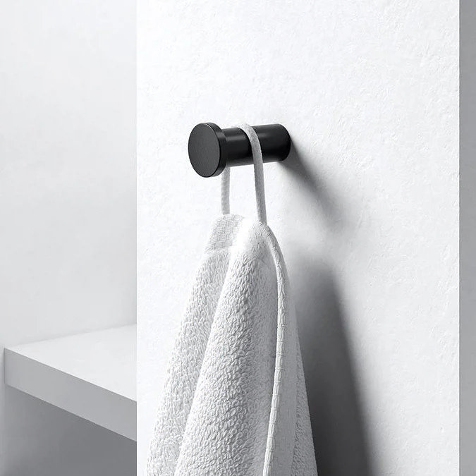 Black wall-mounted bathroom hook holding a white towel against a minimalist wall
