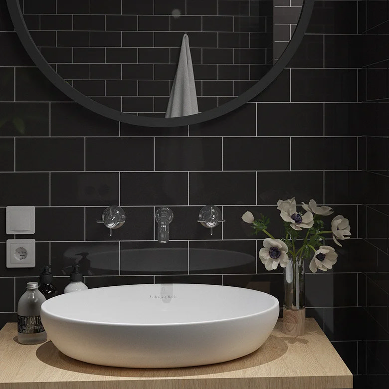 Bathroom vanity with black gloss metro tiles, round mirror and white vessel sink on a wooden countertop.