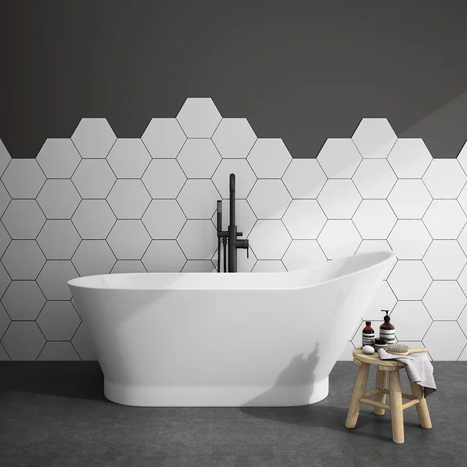 Freestanding Toreno slipper bath with black floor-mounted tap, set against white hexagonal tiles and dark grey upper wall—styled with wooden stool and modern spa accessories