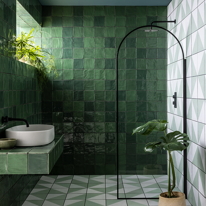 Modern bathroom featuring deep green gloss tiles, a black-framed walk-in shower, geometric patterned flooring, and lush indoor plants, creating a bold yet tranquil wet room design.