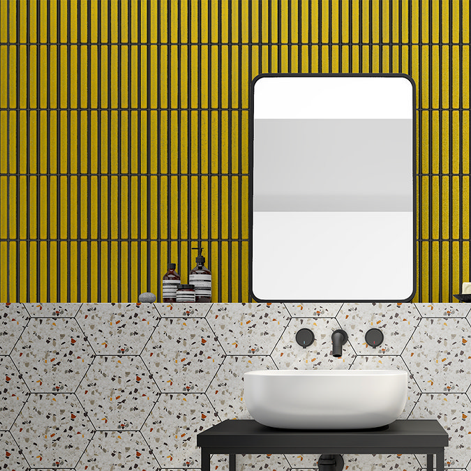 Modern bathroom with vibrant yellow vertical wall tiles paired with hexagonal terrazzo tiles, featuring a white basin and black fixtures, creating a bold, contemporary design.