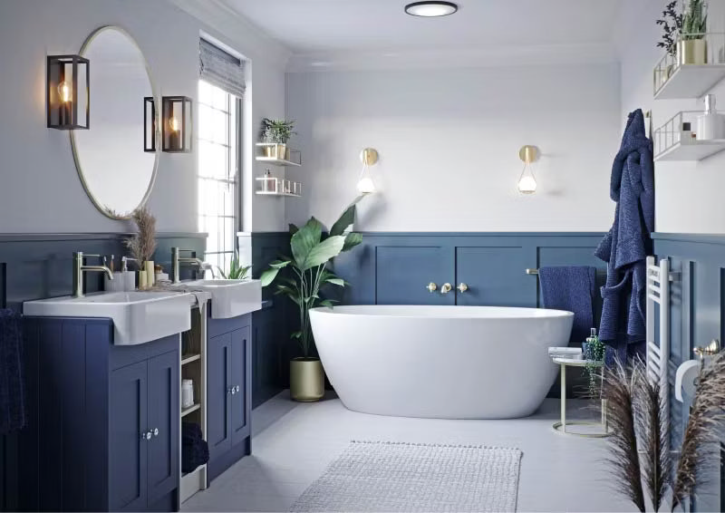 Modern bathroom with blue wood panelling, freestanding white bathtub, and twin sinks. Features elegant lighting, indoor plants, and gold fixtures for a stylish finish.