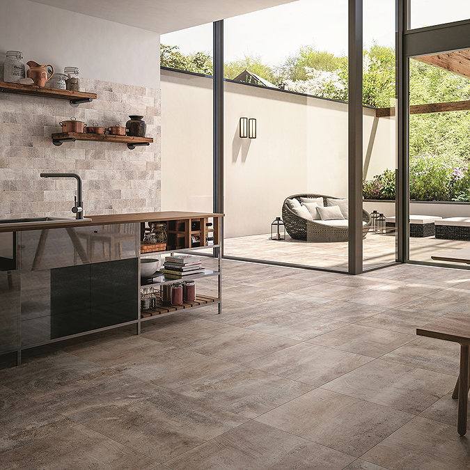 tone-effect floor tiles in a modern open-plan kitchen with large glass doors leading to a patio seating area, creating a seamless indoor-outdoor flow.