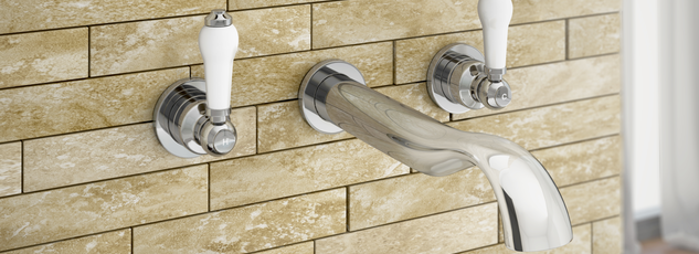 Traditional wall-mounted chrome bath mixer tap with white ceramic lever handles on a beige brick-style tiled wall