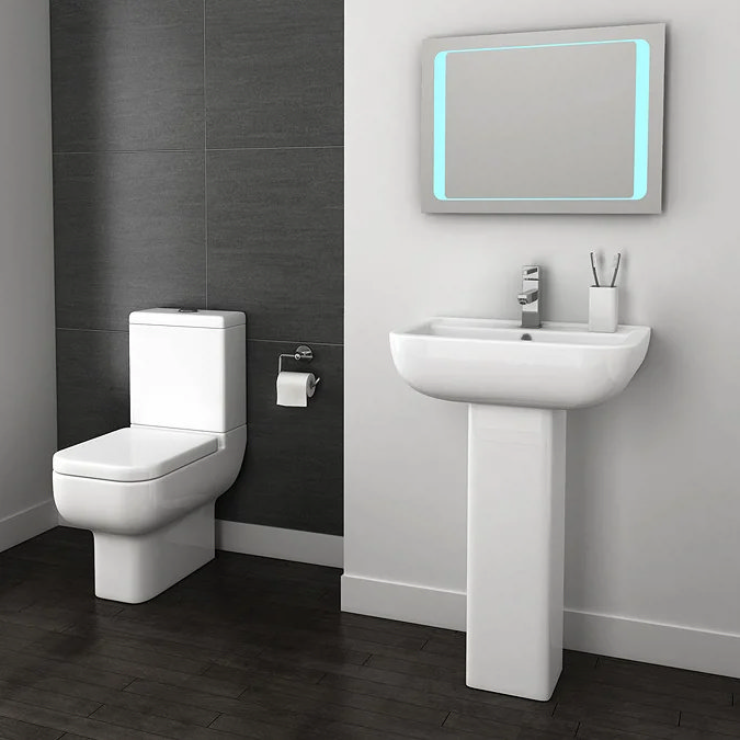 Minimalist bathroom featuring a sleek white toilet and pedestal sink set against contrasting dark wall tiles, with a modern LED-lit mirror adding a futuristic touch.